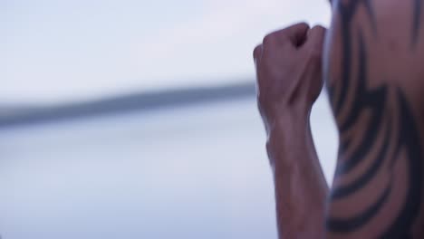 man with tattoo practicing boxing by the lake