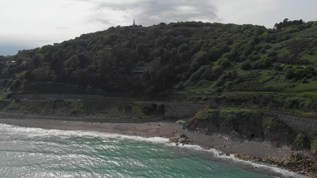 Veduta aerea di Kiliney Hill dal Mar d'Irlanda in una giornata di sole splendente, con onde che si abbattono sulla riva.