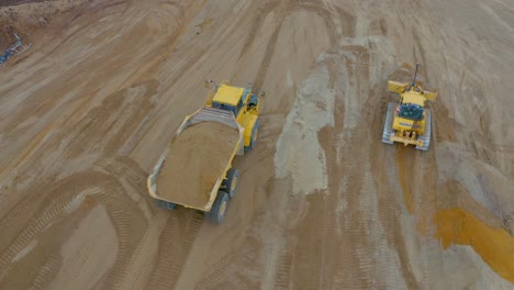 Articulated-hauler-dump-truck-filled-with-sand-driving-past-bulldozer,-mine