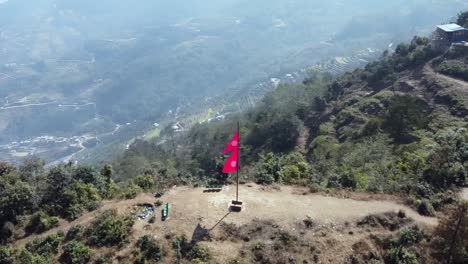 an aerial spiraling view of a nepal flag posted on the top of a hill in the himalaya foothills in nepal