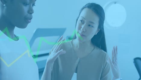 animation of data processing over two diverse women discussing over a digital tablet at office