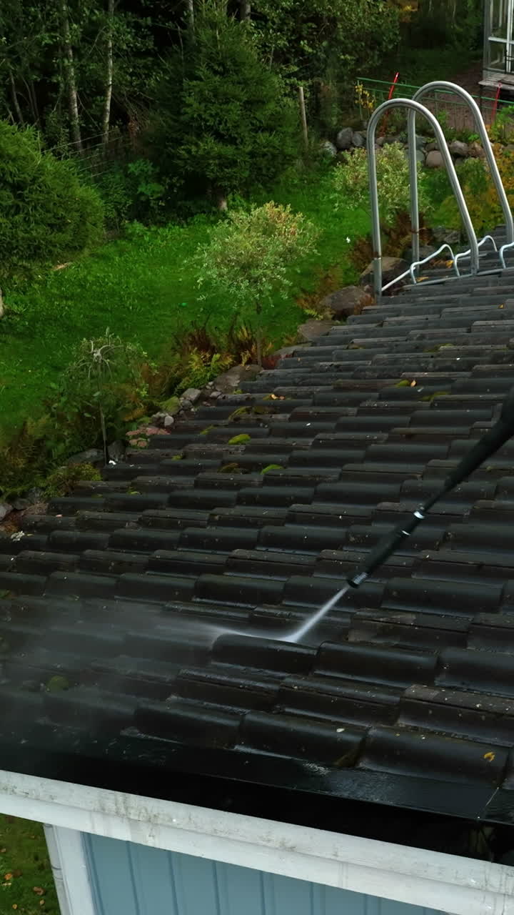 Vertical drone closeup of a woman washing a house roof, sunny, autumn day