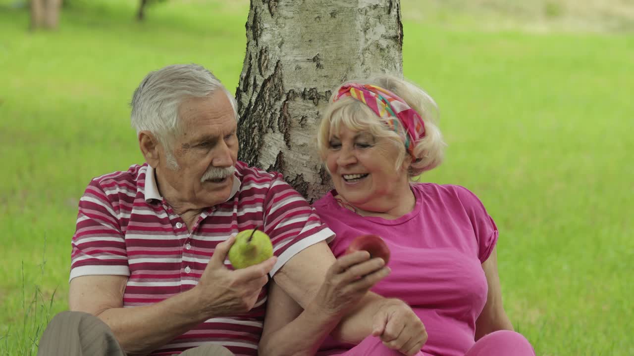 Pic-nic di famiglia nel fine settimana al parco. Coppia anziana caucasica attiva seduta vicino a un albero che mangia frutta.