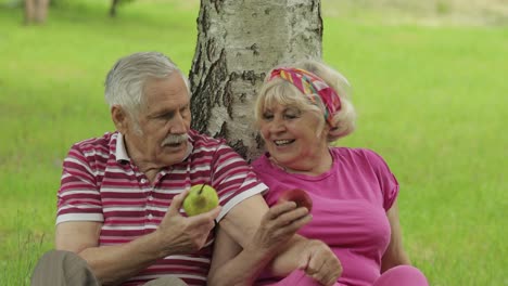 Family-weekend-picnic-in-park.-Active-senior-old-caucasian-couple-sit-near-tree-and-eating-fruits