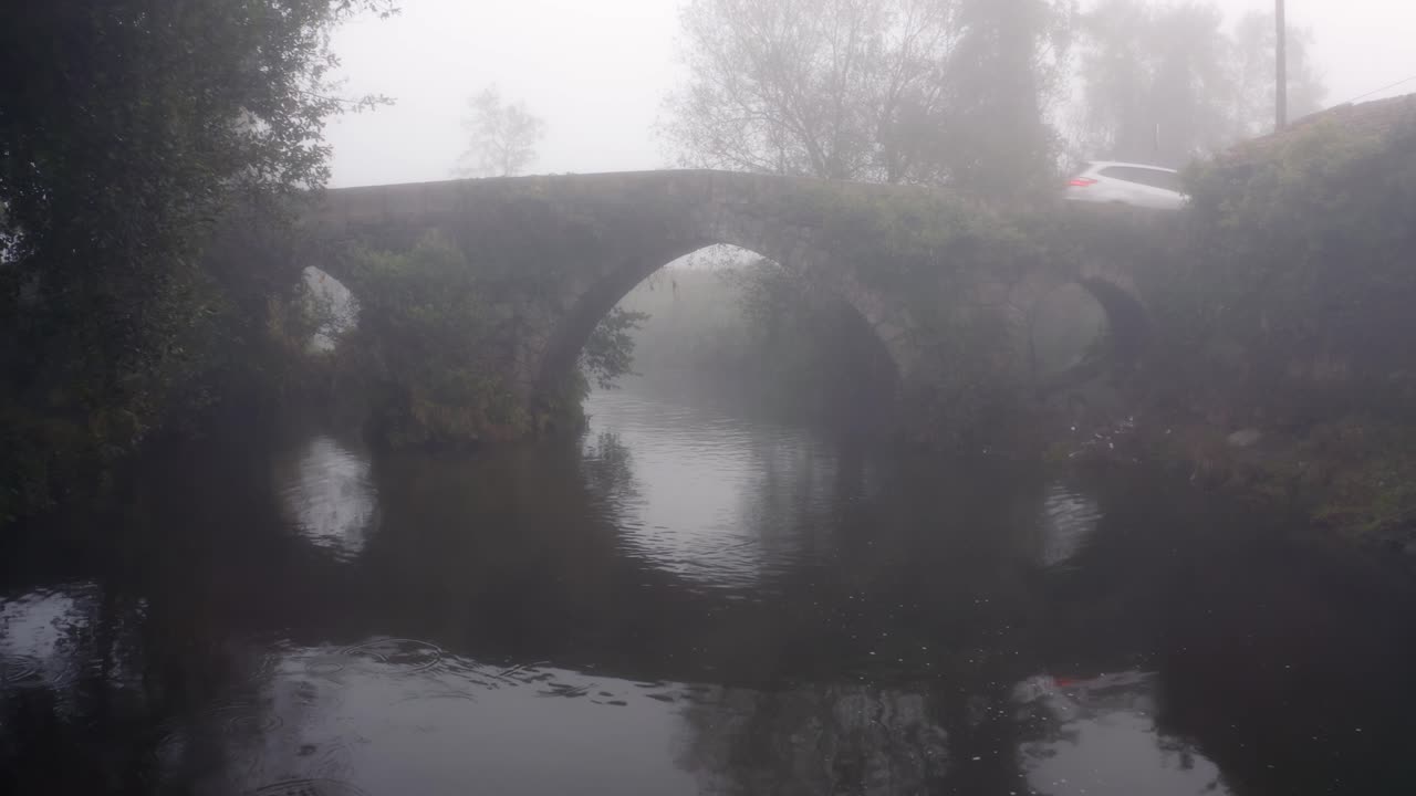 White Car Driving Across Stone Arch Bridge On A Misty Morning In Portugal
