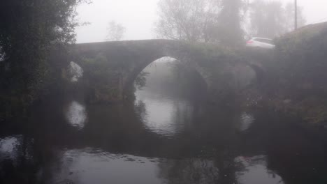 white car driving across stone arch bridge on a misty morning in portugal