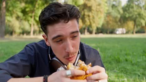 un joven comiendo un sándwich en un parque