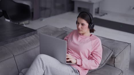 Mujer-Que-Trabaja-Con-Una-Computadora-Portátil-Y-Escucha-Música-Con-Auriculares-En-Un-Sofá
