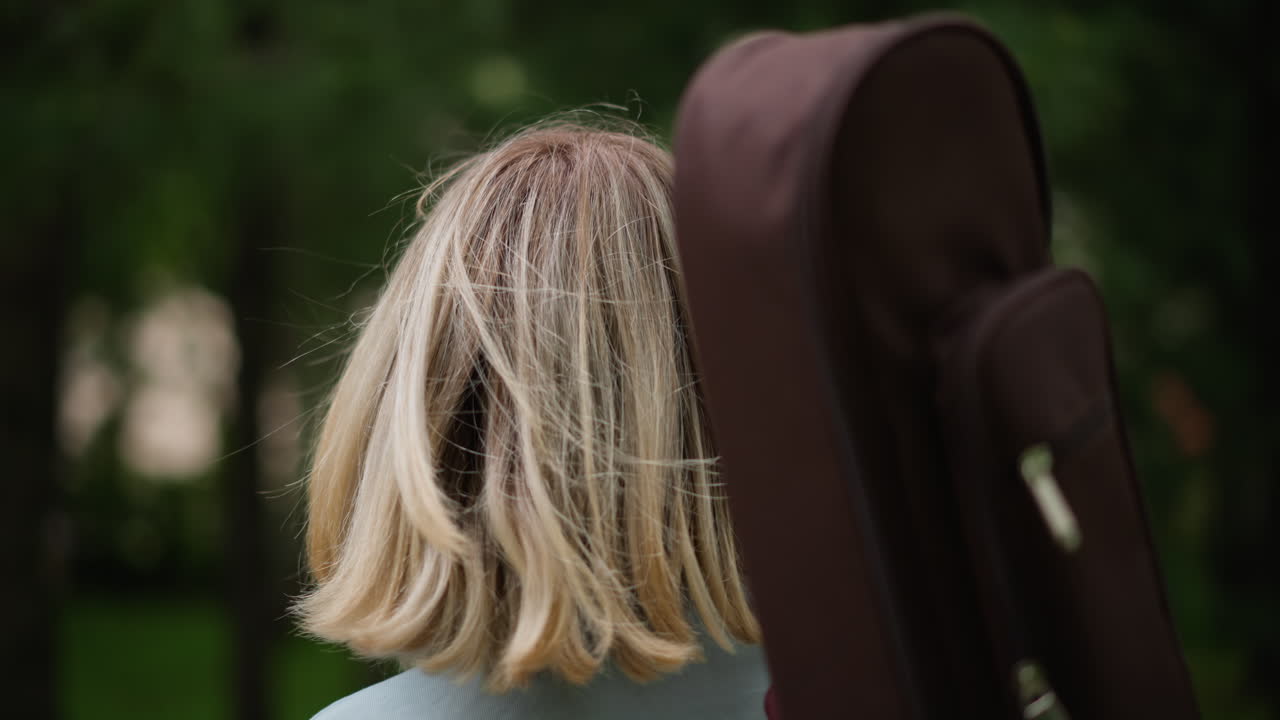 Nahaufnahme eines weißen Gitarristen im Park, Profilansicht, blonde Haare mit Pollen übersät, brauner Koffer auf der Schulter, nachdenklicher Blick, weiche Bokeh-Bäume, introspektive Indie-Stimmung, Ruhe vor dem Auftritt