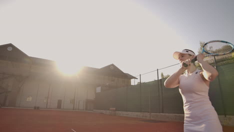 Cheerful-athlete-waiting-for-tennis-ball.-Skillful-female-tennis-player-is-preparing-to-beat-a-ball.-She-is-holding-a-racket-and-posing.-Woman-is-standing-on-tennis