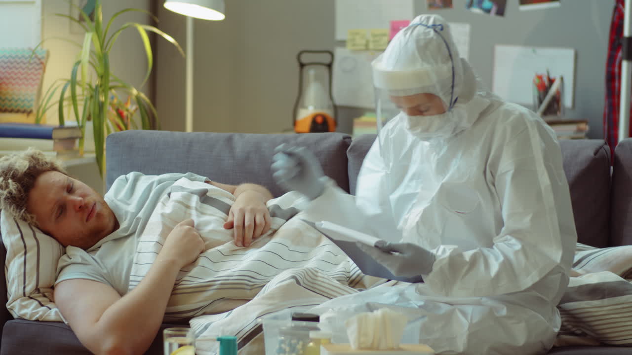 врач измеряет температуру пациента с коронавирусом и сообщает план лечения