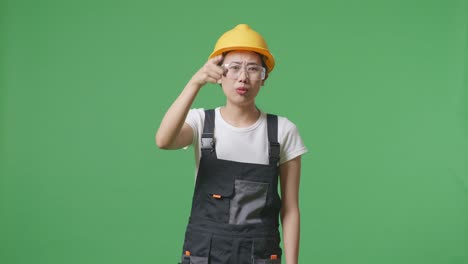 asian woman worker wearing goggles and safety helmet shouting to camera while standing in the green screen background studio