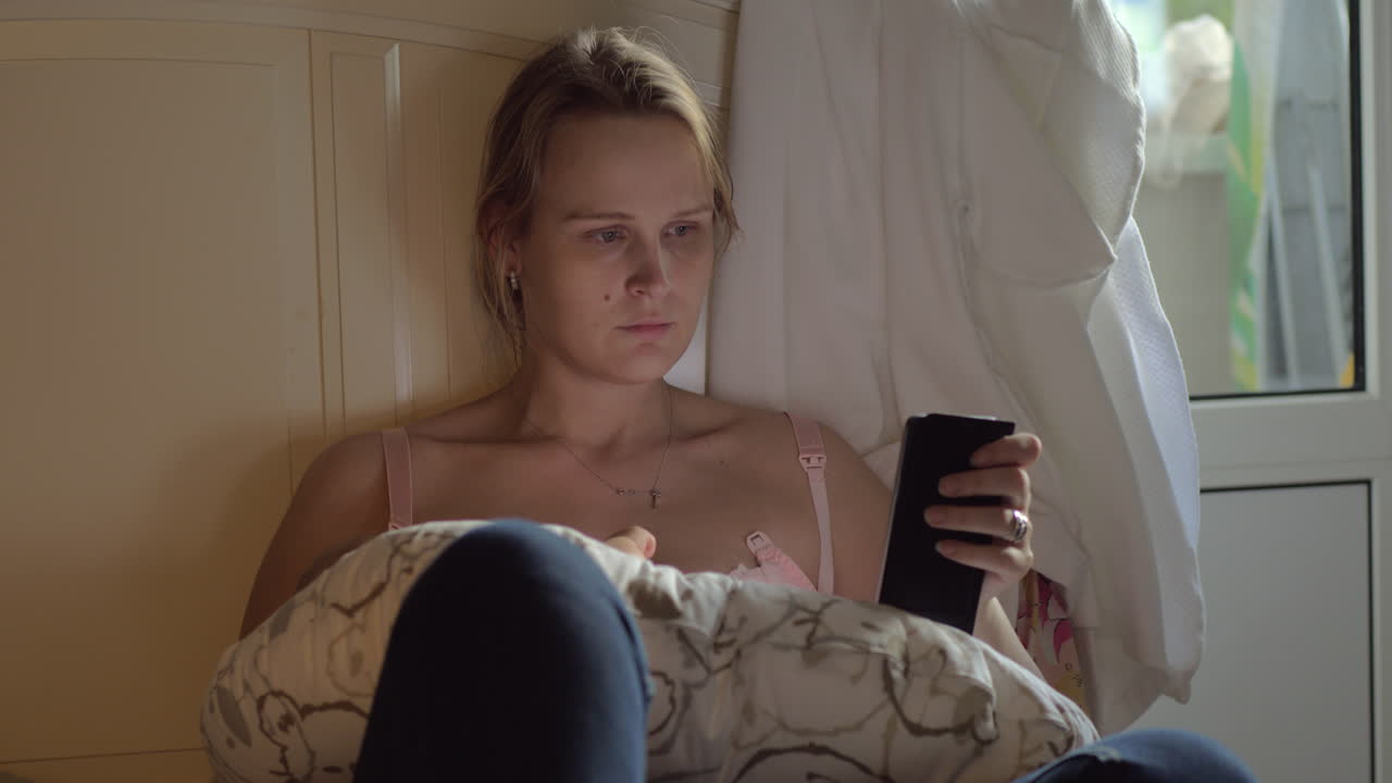 Mulher amamentando bebê e navegando na internet no celular