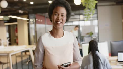 portrait of african american casual businesswoman using smartphone laughing at office, slow motion