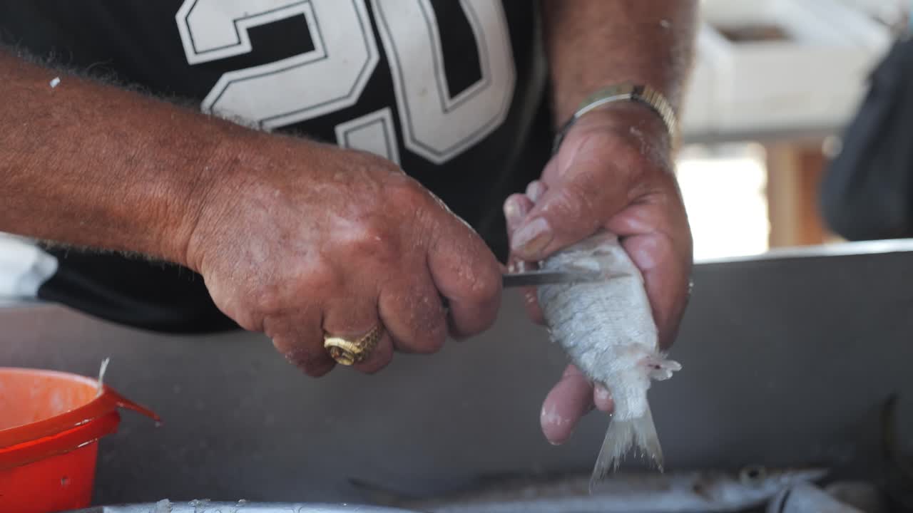 primer plano de un pescador raspando las escamas de un pescado fresco mientras aún está en el barco