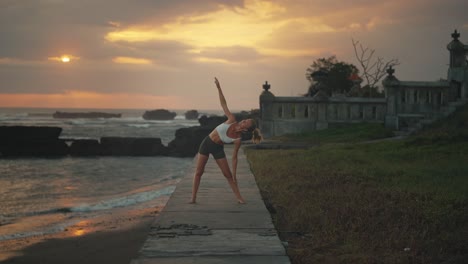 woman doing triangle pose with dramatic sunset in background, bali coast