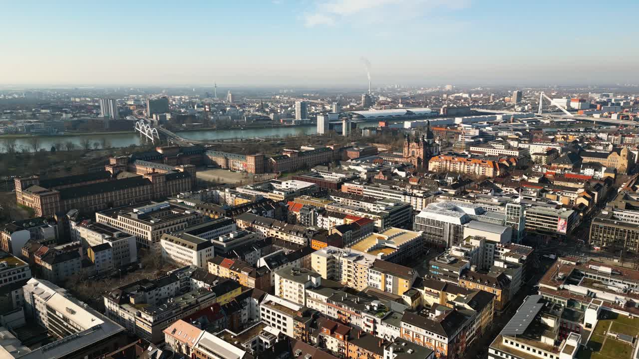 Drone flight over Mannheim's downtown towards the castle, Jesuitenkirche, Rhine River, and Ludwigshafen on a sunny day.