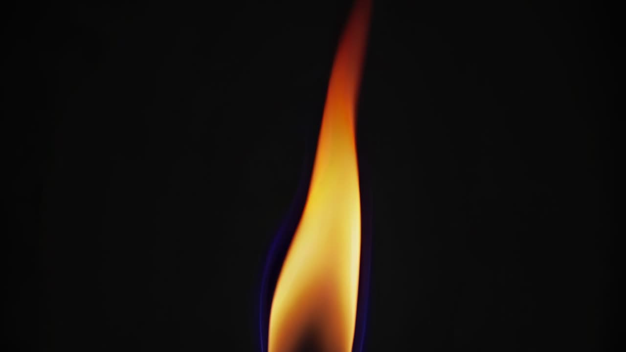 Close-up video of a single flame against a dark background, captured from a side angle