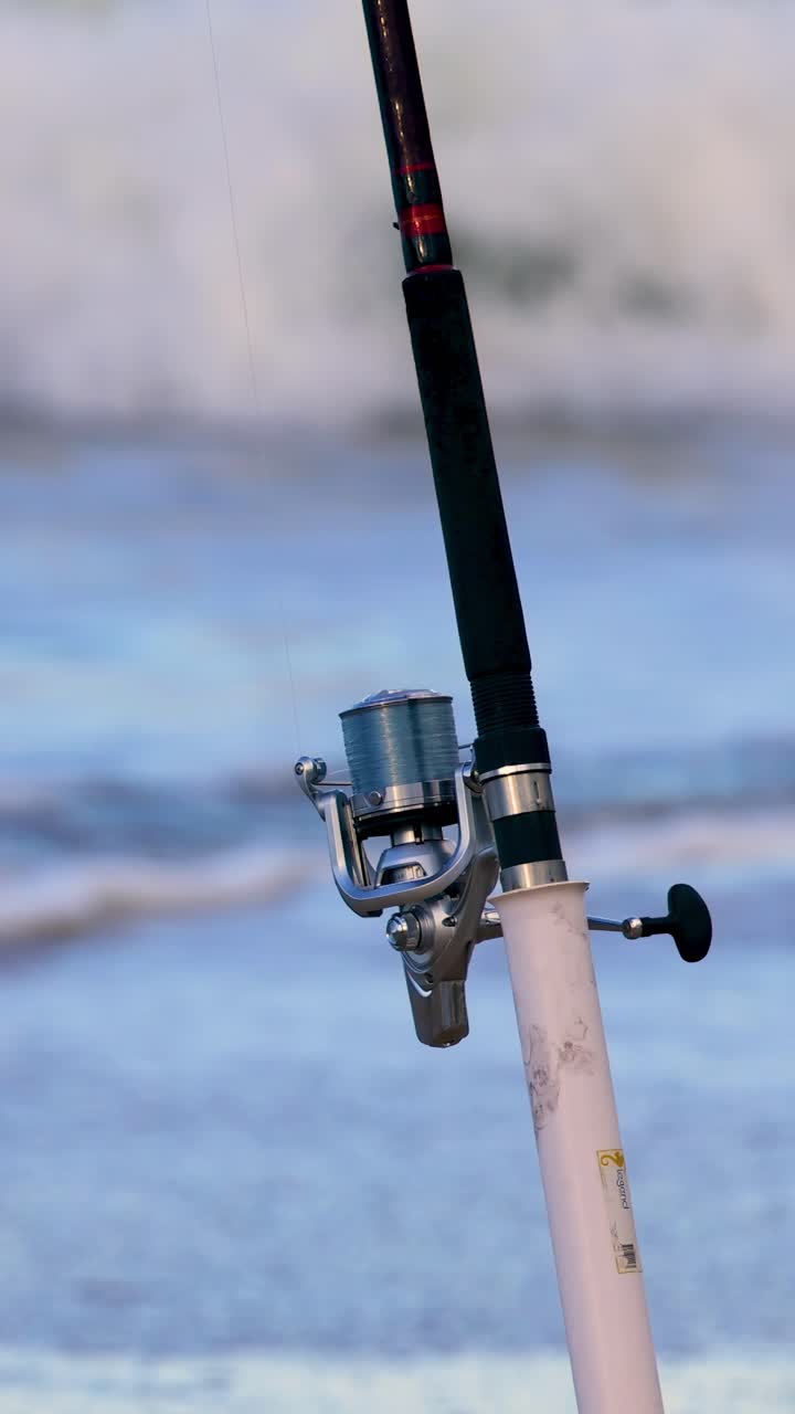 Una canna da pesca si erge sullo sfondo di onde oceaniche, catturando la serena atmosfera costiera al crepuscolo.