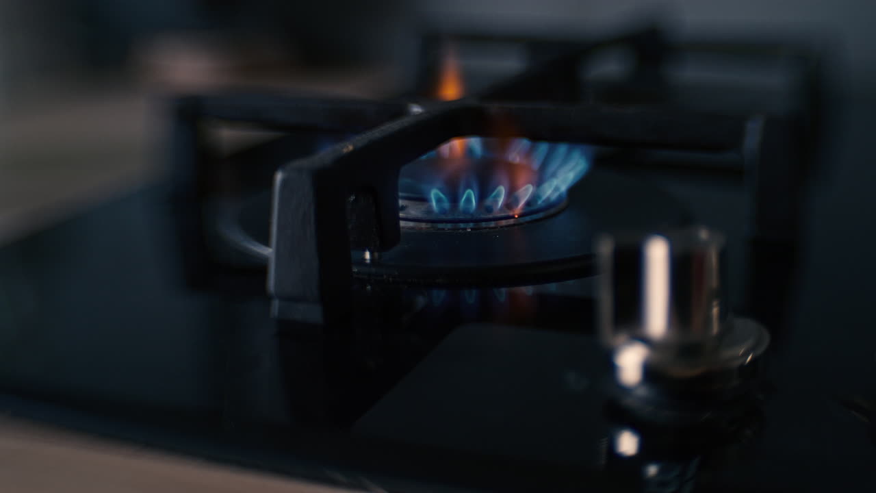 A distorted shot of a black ceramic gas stove hob being lit, the fire burns for a while, and is then turned off