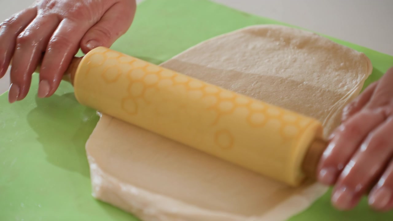 Escena de cocina desde arriba mostrando manos presionando y alisando masa enrollada sobre una tabla verde brillante, dando forma a una masa suave para preparar la cocción con un toque cuidadoso, superficie limpia y luz natural.