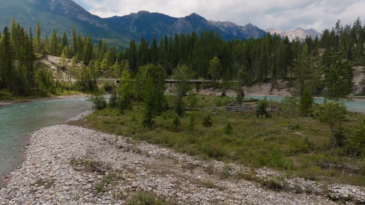 Ripresa a bassa quota con drone sopra il fiume Kootenay che rivela un ponte con le Montagne Rocciose sullo sfondo nella Columbia Britannica, Canada
