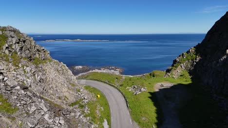 drone follows a winding road through the mountains of værøy, opening to a stunning view of the ocean and distant lofoten islands