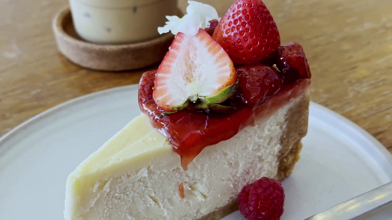Primo piano di una fetta classica di cheesecake newyorkese con una consistenza cremosa e una crosta dorata, servita su un piatto bianco per una deliziosa presentazione del dessert