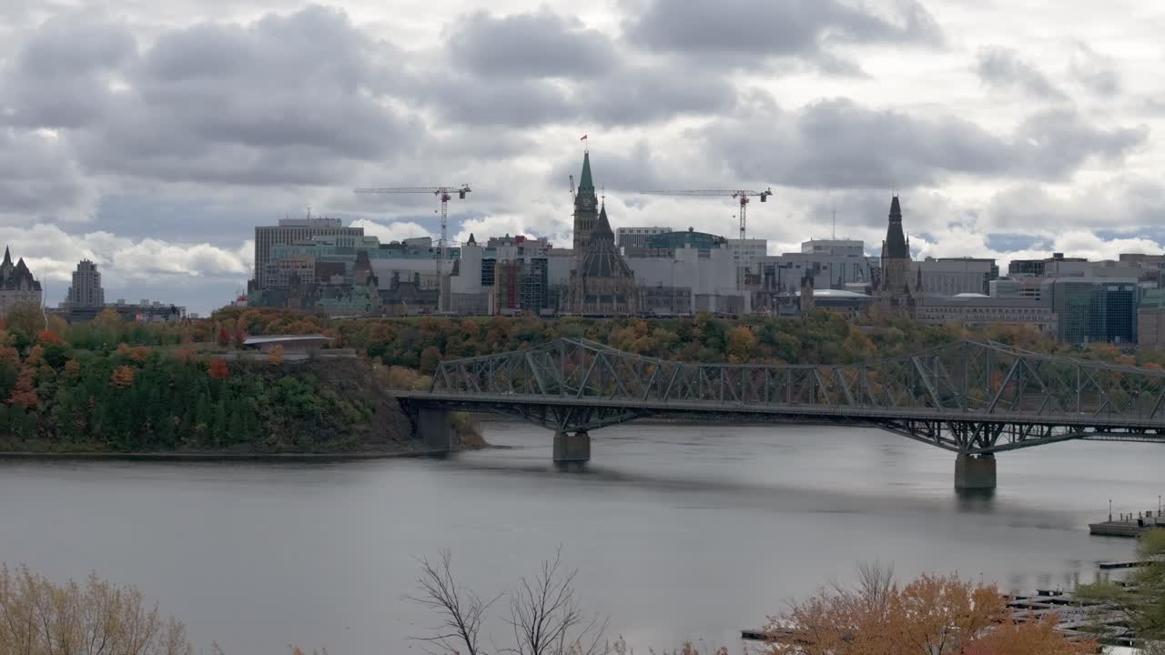Views of Parliament Buildings with Alexandra Bridge and Ottawa River in foreground in fall on a cloudy day