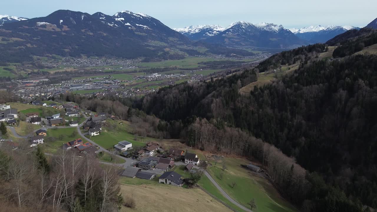 drone se levanta y revela una vista increíble sobre el paisaje urbano rodeado de cumbres cubiertas de nieve en amerluegen, vorarlberg, austria