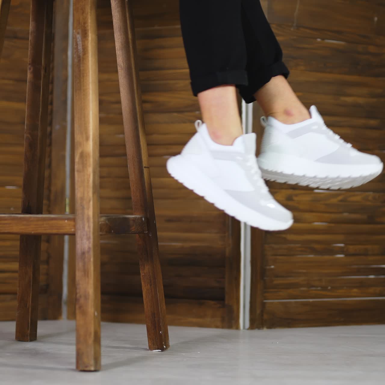 Unrecognizable woman sitting on a high wooden stool and waving feet. Model demonstrates white comfortable footwear