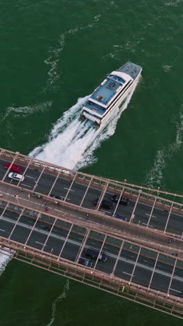 big city bridge with transport traffic roads and pedestrian zone. white yacht sailing under the bridge. top view. vertical video