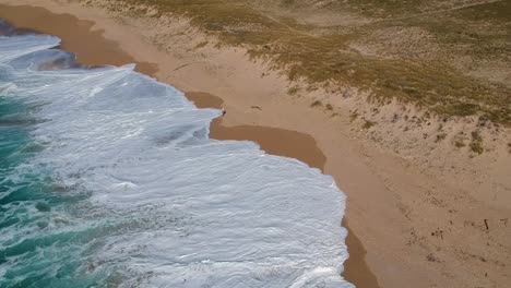 Lone-man-walking-on-sandy-beach-and-get-splashed-by-sea-wave