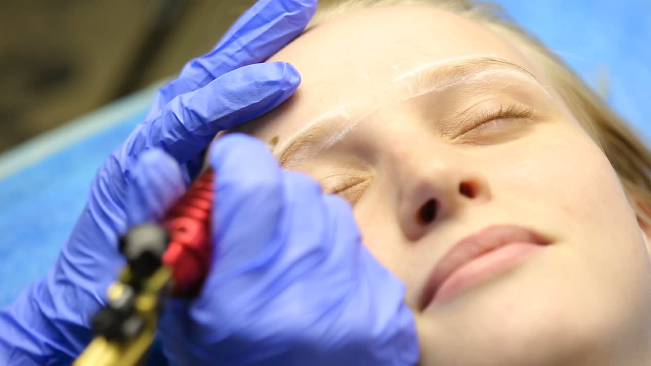 Beautician hands doing eyebrow tattoo on woman face
