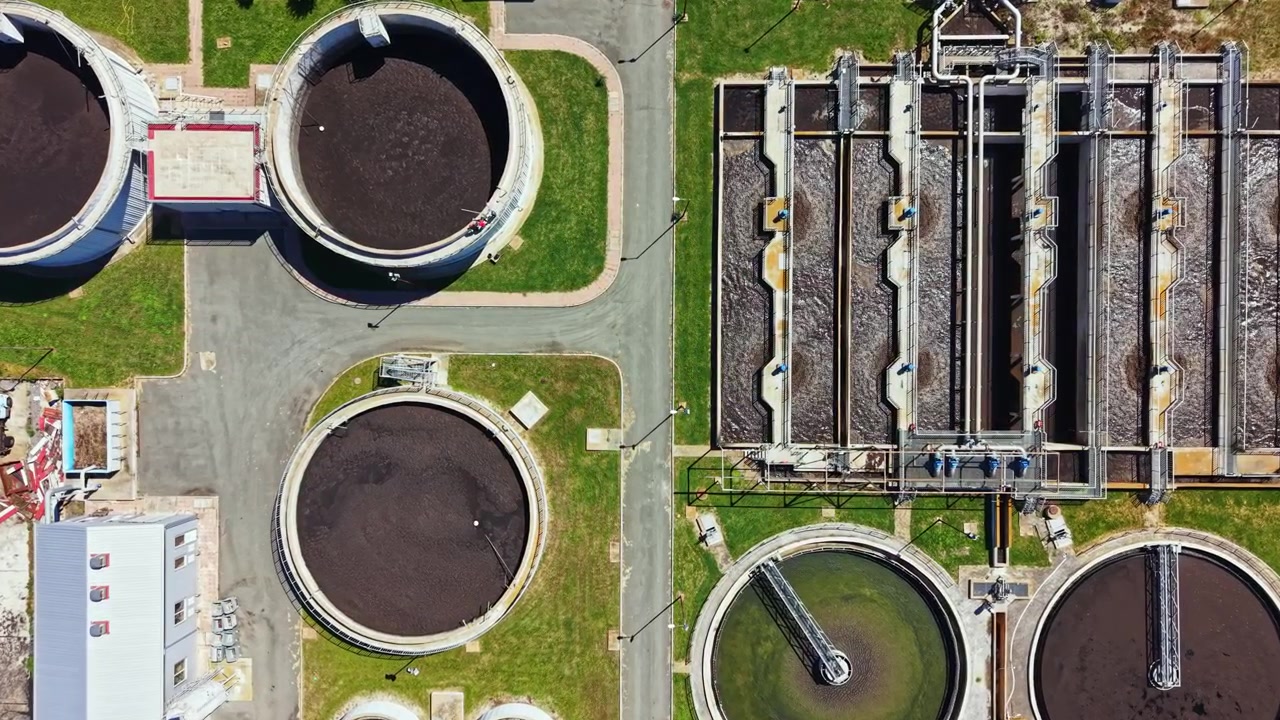 Wastewater treatment facility in operation, showing multiple large tanks and treatment processes from above during daytime hours