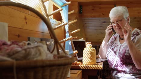 Front-view-of-old-caucasian-senior-woman-talking-on-mobile-phone-and-sitting-at-desk-in-workshop-4k