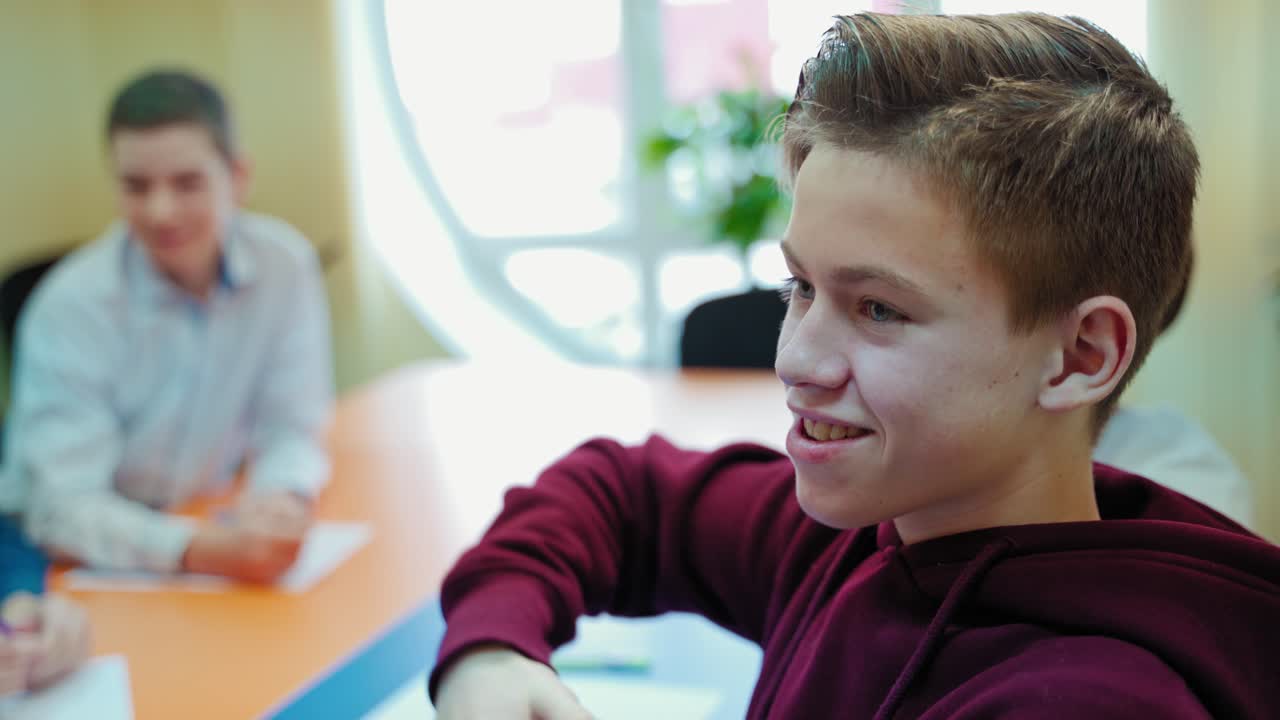 Teenage boy in the classroom. Student sitting at the table and talking to the teacher at school. Creative thinking of a pupil. Education concept.