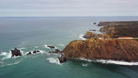 Praia-Da-Arrifana-Klippen-Im-Westen-Portugals-Mit-Bewölktem-Himmel,-Luftaufnahme-Der-Umlaufbahn