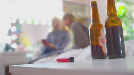 dos adolescentes en el dormitorio con botellas de cerveza y bolígrafo de vape en primer plano