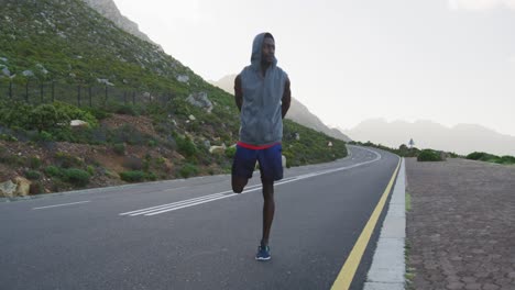 African-american-man-wearing-a-hoodie-performing-stretching-exercise-on-the-road