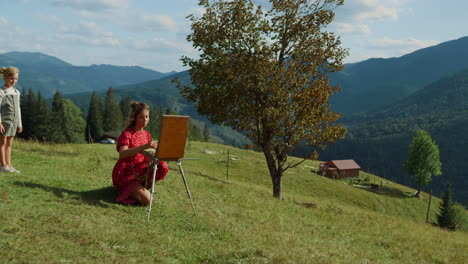 mujer creativa dibujando en las montañas. niña observando el proceso de pintura.