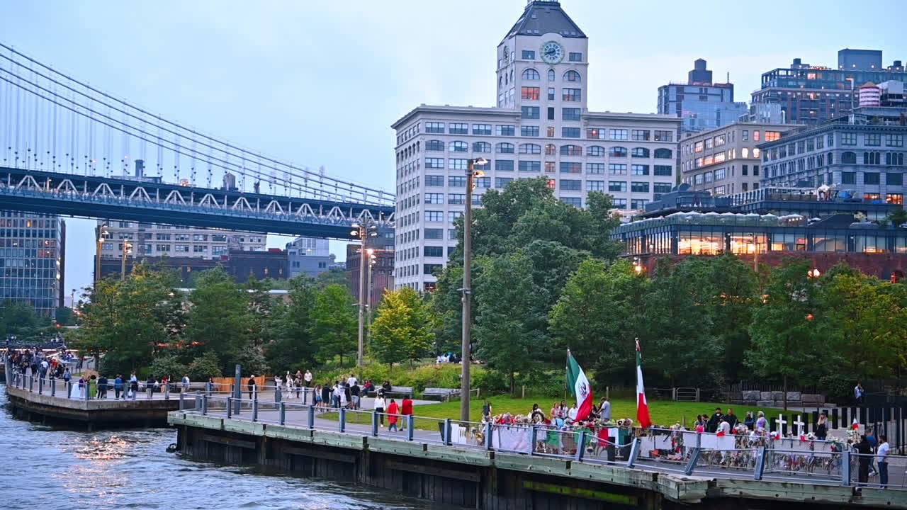 People walk by the quay of the river in New York, USA. Stunning buildings and the Manhattan Bridge at backdrop