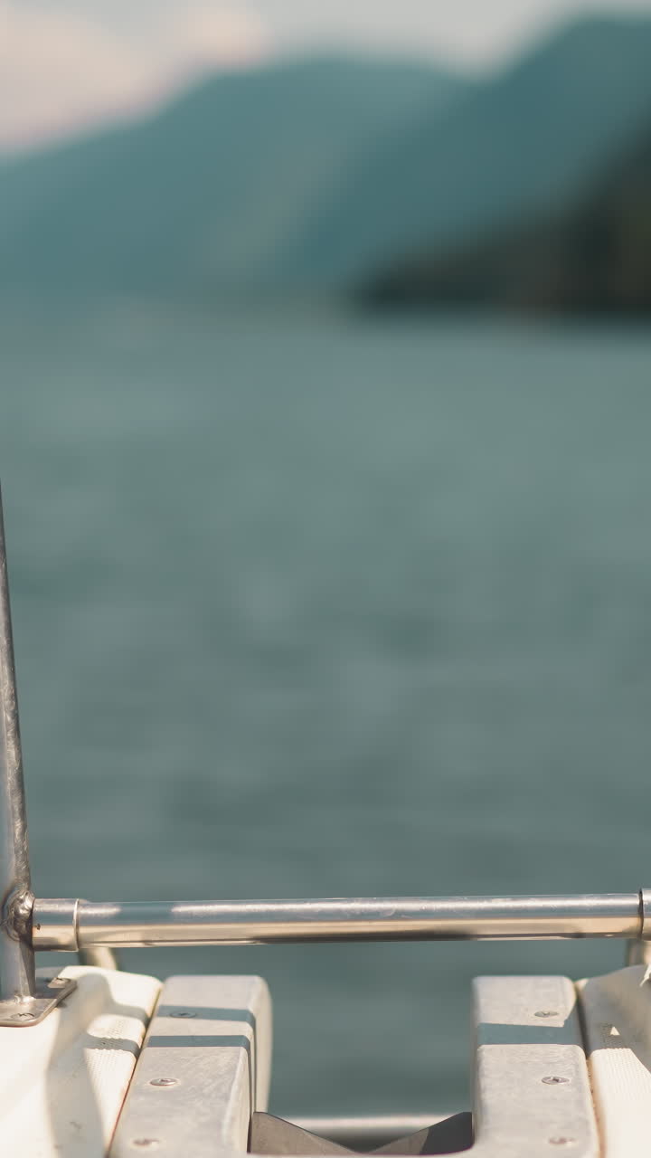 Stern with metal handrails on deck of sailing motor boat in sea against blurry mountains closeup. Back part of modern yacht with railings in ocean bay