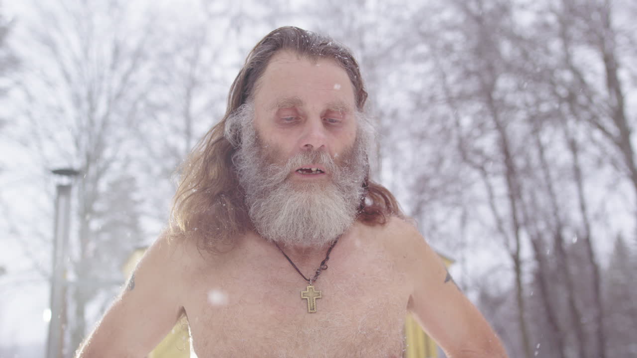 Spiritual scraggy man with Christian cross necklace bare chested in snow flurry