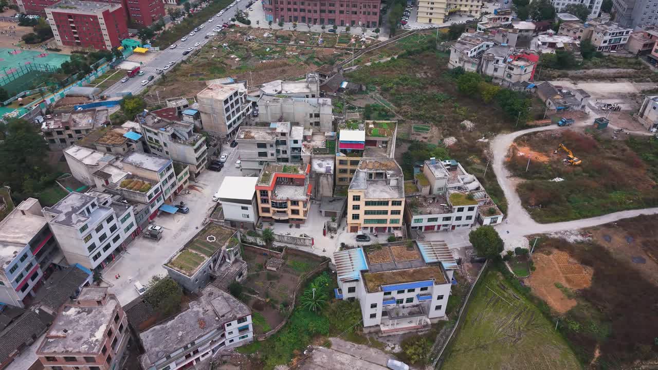 Orbiting drone shot of Huishui’s suburban edge, contrasting older low-rise homes, small farmland plots and expanding high-rise developments, China