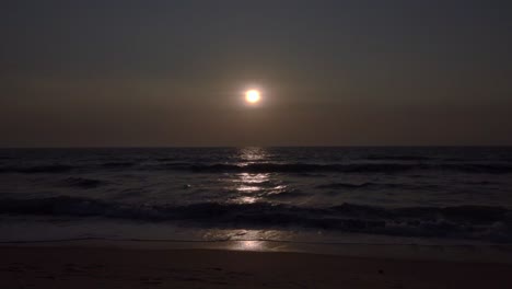 puesta de sol con poca luz con el mar en primer plano mientras las olas golpean la playa