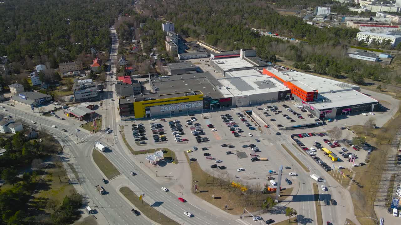 Aerial drone footage orbiting and spinning around a large yellow and white colored shopping mall called järve keskus during a sunny spring or autumn day. Cars driving on Tallinn Pärnu highway as well.