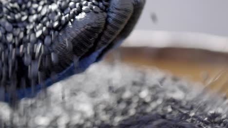 manos con guantes de protección levantan gránulos de polímero negro en una planta de reciclaje de basura de primer plano