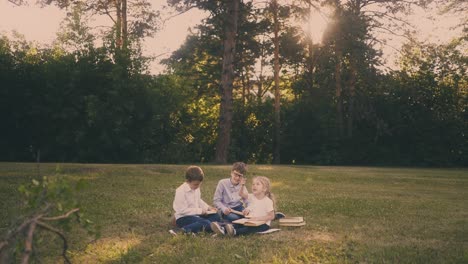 schoolboys-with-girl-do-home-task-reading-books-on-grass