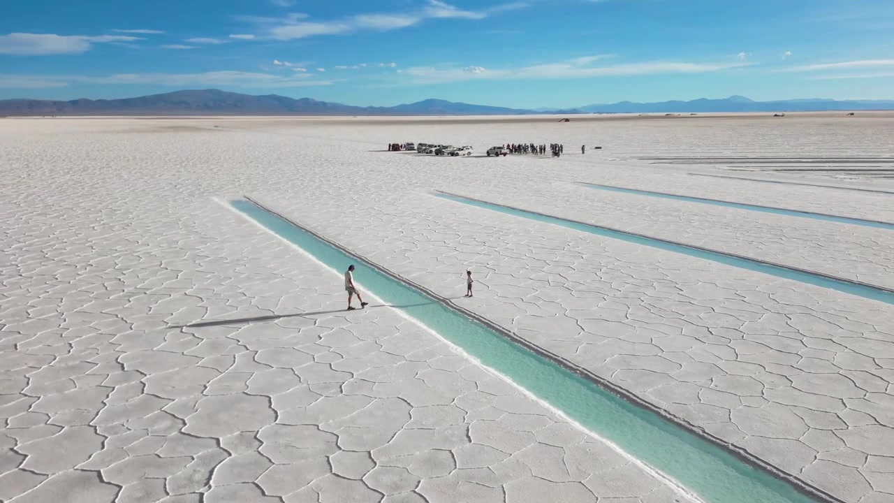 Aerial View of People Walking on a Vast Salt Flat with Turquoise Water Channels